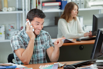 Obraz premium man pointing on a computer while talking on the cellphone