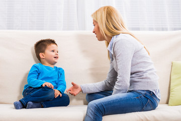 Mother and son sitting on sofa and talking about something.