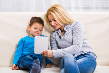 Mother and son are sitting on sofa and using digital tablet.