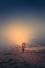 Lonely hiker  with backpack walking along the trail on the mountain top at foggy day time. Travel lifestyle concept.