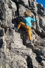 Little boy climbing a rock face. Outdoor activity and recreation.
