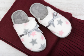 Pair of warm slippers and red scarf on a white wooden background