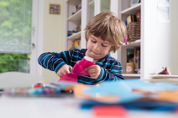 Cute litle boy cutting shapes out of colored paper. Children being creative, developing imagination, creativity, do it yourself concept - obrazy, fototapety, plakaty