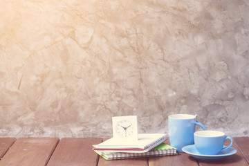 Two blue cups of coffee on wooden table with alarm clock and not