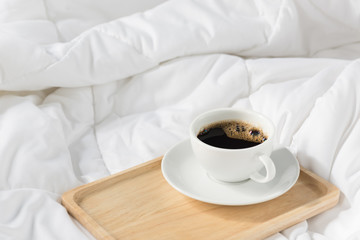 Cup of coffee with wooden tray on bed background