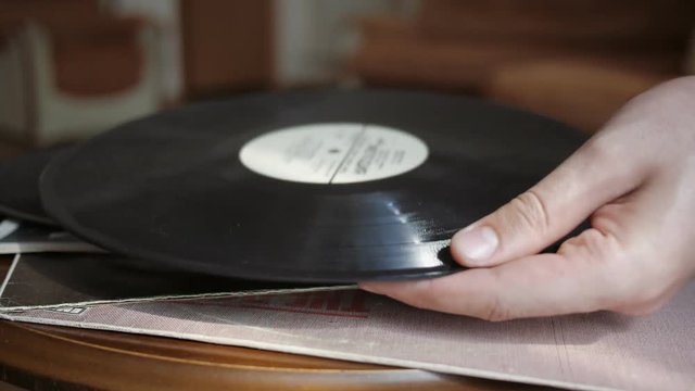 Male hands take the vinyl record from the table to listen the music. Retro records on the table. Close up.