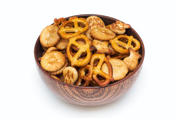Mix of salty snacks (crackers and pretzels) in wooden bowl isolated on white background