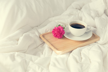 Fototapeta na wymiar Cup of coffee and pink rose flower with wooden tray on bed backg