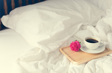 Cup of coffee and pink rose flower with wooden tray on bed backg