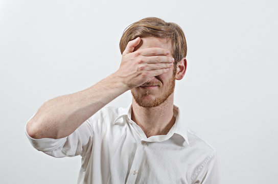     Young Adult Male Wearing White Shirt Covers His Face by Hand, Gesturing He Has Made a Big Mistake 
