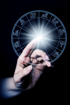 woman hand touching a light with rays in zodiac wheel with astrology symbols
