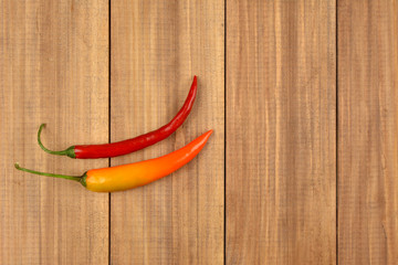 Two fresh chili pepper on brown wooden background.