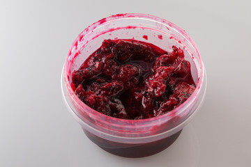 Black currant jam in the plastic container on white background