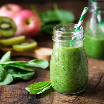 Green detox smoothie with spinach, kiwi and apples in a jar with a straw on dark rustic wooden background