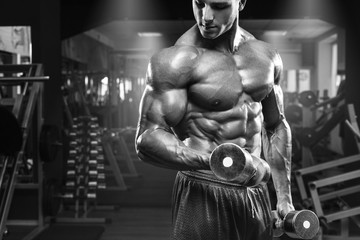 Fototapeta na wymiar Muscular man working out in gym doing exercises with dumbbells at biceps, strong male torso abs