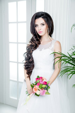 gorgeous bride in luxury wedding dress. Bride. Perfect Make up and Long Wavy Hair. Hairstyle, wedding  jewelry. Beautiful Woman with Shiny Brown Hair. gorgeous wedding bouquet of various flowers.