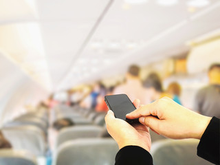 Businessman is using / touching mobile phone over blurred passengers and seats in an commercial airplane