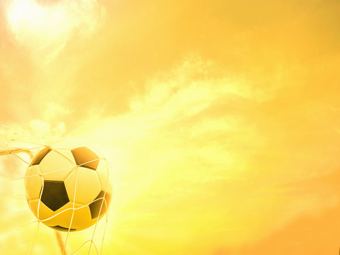Football in goal net with warm yellow sky background