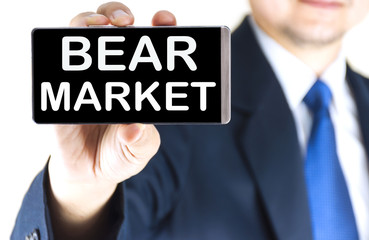 BEAR MARKET word on mobile phone screen in blurred young businessman hand over white background, business concept