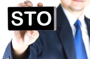 STO word on mobile phone screen in blurred young businessman hand over white background, business concept