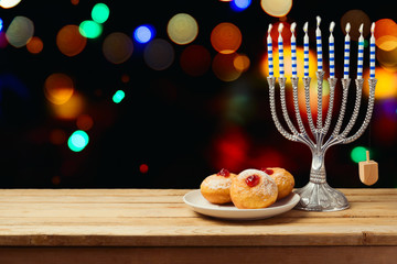 Hanukkah holiday sufganiyot with menorah on wooden table over night bokeh background