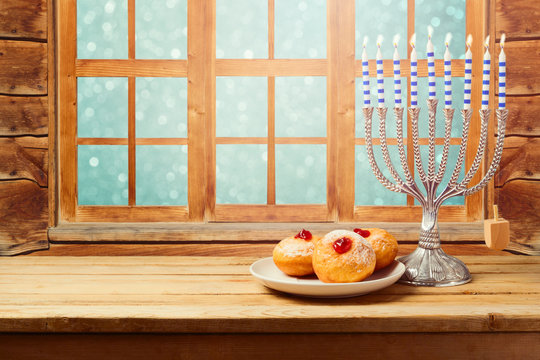 Hanukkah holiday sufganiyot with menorah on wooden table over window background