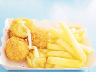French fries and fried cheese balls in paper container over blue