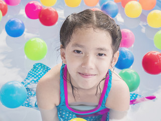 Fototapeta na wymiar Asian kid is playing in a kid water pool with colorful balls