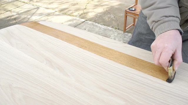 Carpenter is covering wooden table by lacquer. Worker making furniture and toning wood by paint
