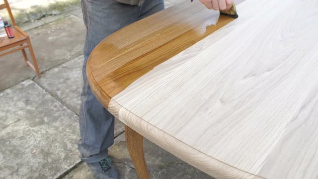 Carpenter is covering wooden table by lacquer. Worker making furniture and toning wood by paint