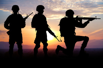 Silhouettes of soldiers on sunset background. Military service concept.