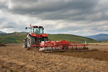 Naklejka premium Farmer in tractor preparing land with seedbed cultivator