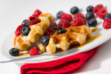 Close-up of waffles with berries and maple syrup on a white plat