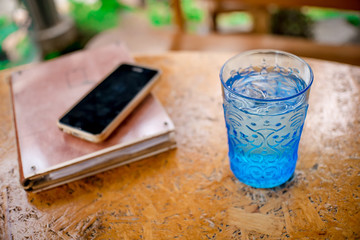 Blue Glass with water Notebook and Smartphones on a wooden table.