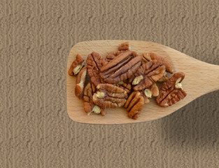 Wide rectangular wooden spoon filled with pecan halves, against tan texture fill background- healthy eating concept with lots of copyspace