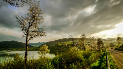 Scenic lake, hills, sunset beams and stormy clouds in the valley