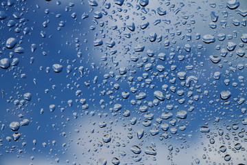 Rain drops on window with blue cloudy sky in background , spring rainy day