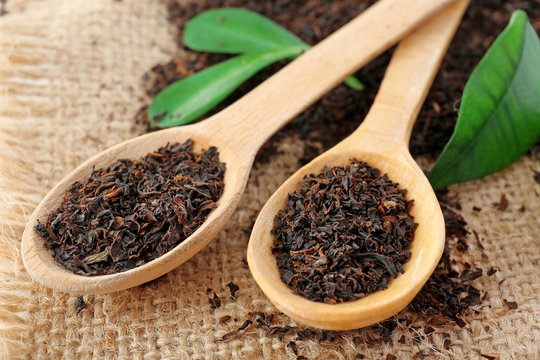 Black dry tea in wooden spoons on bagging
