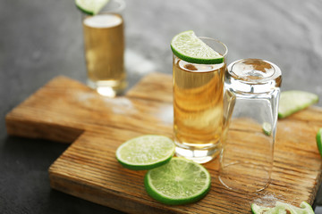 Empty glass, shot with golden tequila and lime on wooden cutting board