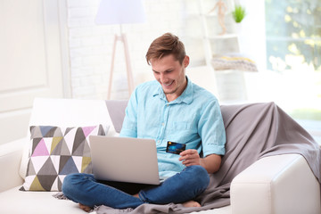 Young happy man with laptop and credit card making online shopping
