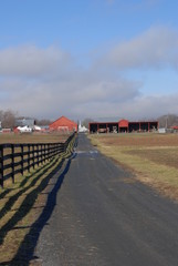 Obraz premium Fence along a road takes you to a red barn and farm under pink clouds