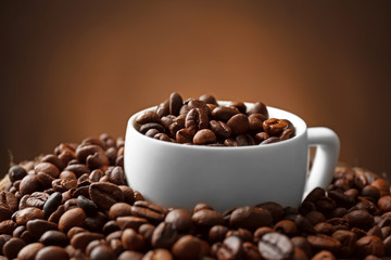 Sack with roasted coffee beans and white cup on dark background, close up view