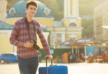 Young man with big blue trunk and camera standing on the street