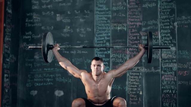 Muscular topless young man doing weightlifting exercises in cross fit gym.