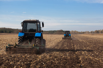 Fototapeta premium The sloping field. Two large blue traktor plow plowed land after harvesting the maize crop on a sunny clear autumn day.
