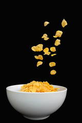 Cereal or corn flakes in a bowl on a black background .