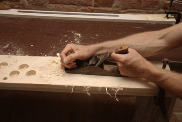 Closeup male hands working at a wooden plank using a carpenter's plane in a workshop