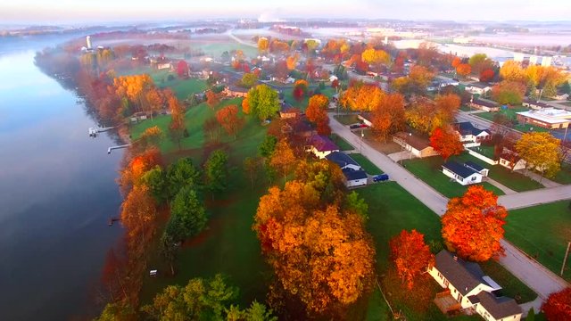 Scenic riverside small town with foggy Autumn sunrise, aerial flyover.
