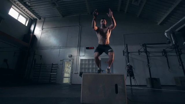 Single shirtless young man in dark shorts in motion doing jumping exercises in large gymnasium