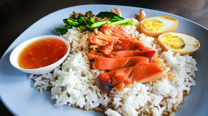 Stewed pork leg on rice  (Kao Kha Moo) with boiled egg garlic and kale in bowl on table.